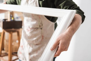 Cropped view of blurred restorer in apron holding wooden picture frame 