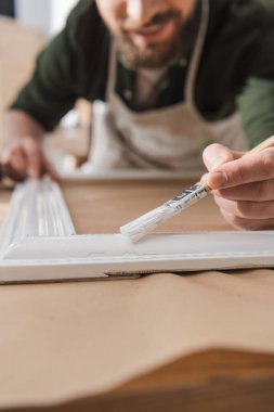 Masaya ahşap resim çerçevesi çizen bulanık restoratörün kırpılmış görüntüsü 
