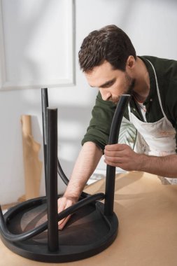 Craftsman in apron polishing black wooden chair in workshop 