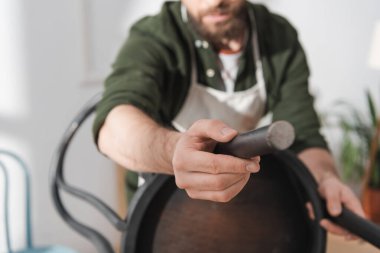 Cropped view of blurred restorer holding wooden chair in workshop  clipart