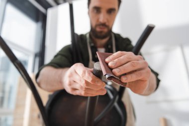 Blurred restorer polishing black chair in workshop 