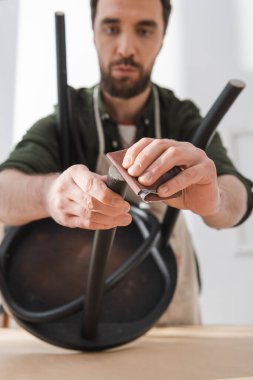 Blurred craftsman sanding part of black chair in workshop 