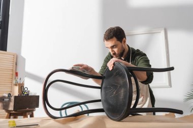 Craftsman sanding paint on wooden chair near square tool in workshop 