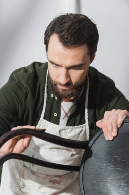 Bearded restorer sanding blurred wooden chair in workshop 