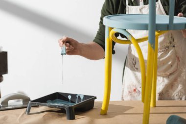 Cropped view of restorer holding paintbrush while painting on chair in workshop 