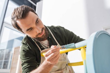 Positive restorer in apron repainting furniture in workshop 