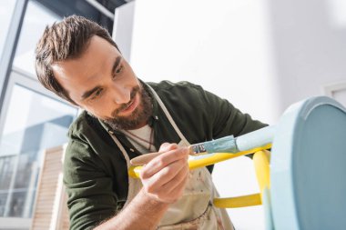 Positive restorer in apron repainting furniture in workshop  clipart