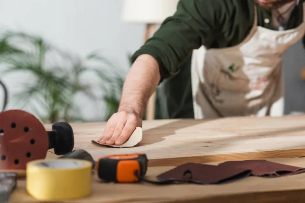 stock image Cropped view of blurred craftsman sanding wooden plank near ruler and masking tape