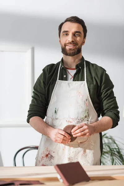 stock image Smiling carpenter holding sandpaper near blurred wooden board in workshop 