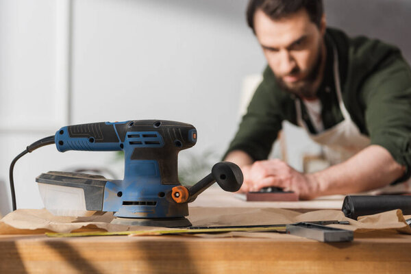 Sanding machine near blurred carpenter working with wooden board 