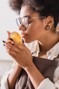 african american craftswoman in eyeglasses smelling bar of scented soap in workshop
