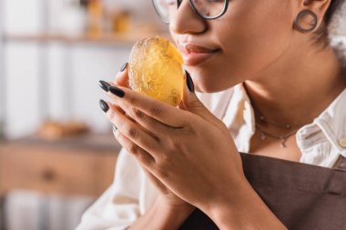 cropped view of african american craftswoman enjoying scent of handmade soap in blurred workshop