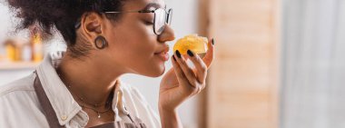 profile of african american woman in eyeglasses smelling aromatic soap in craft workshop, banner