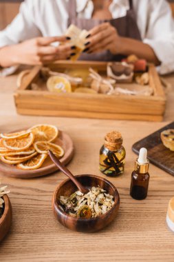 dried herbs and orange slices near essential oils and cropped african american craftswoman on blurred background