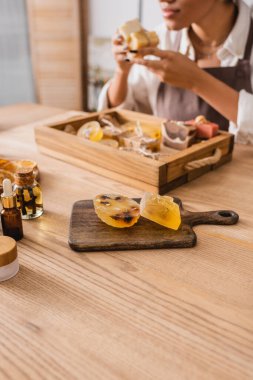 selective focus of handmade soap bars on chopping board near african american craftswoman on blurred background 