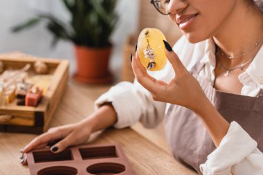 cropped view of smiling african american woman holding herbal soap near silicone mold in craft workshop