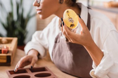 partial view of blurred african american woman holding herbal soap in craft workshop
