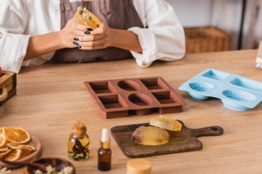 partial view of african american woman holding herbal soap near silicone molds and natural ingredients on blurred foreground