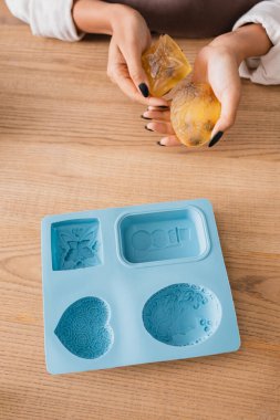 top view of cropped african american craftswoman holding handmade soap near silicone mold on wooden table