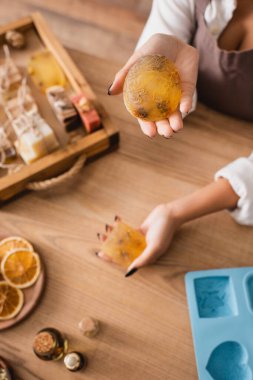 high angle view of african american woman holding homemade soap near silicone mold and natural ingredients on wooden table