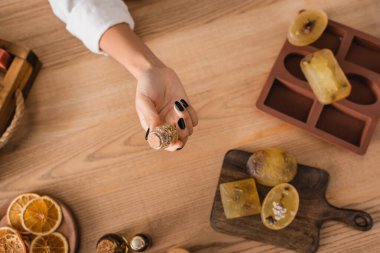 top view of cropped african american woman holding jar with dried herbs near soap bars on chopping board and silicone mold clipart