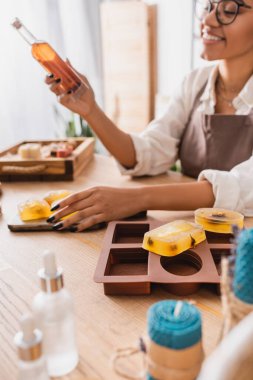 selective focus of handmade soap and silicone mold near happy african american woman with bottle of olive oil on blurred background