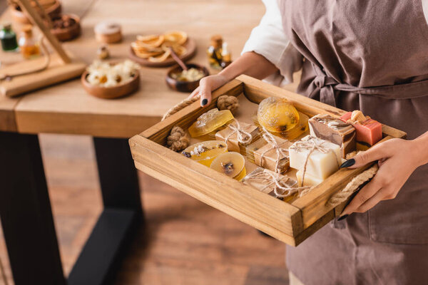 wooden tray with natural handmade soap in hands of african american craftswoman in blurred workshop