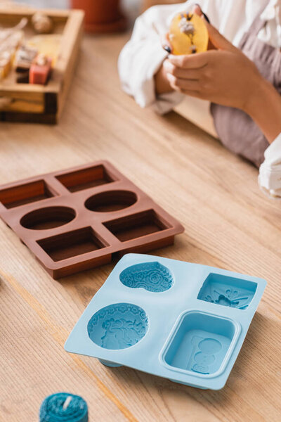 selective focus of silicone molds near cropped african american woman holding handmade soap on blurred background