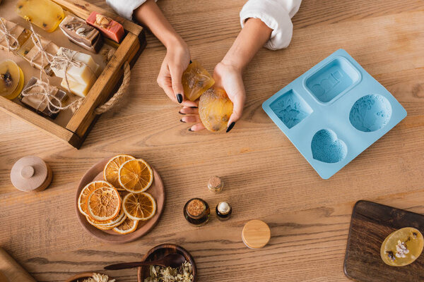 top view of cropped african american woman holding herbal soap near natural ingredients and silicone mold on wooden table
