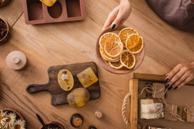 partial view of african american woman holding dried orange slices near homemade soap on wooden tray and chopping board