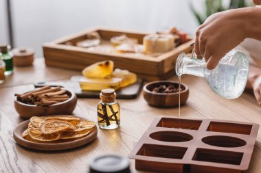 partial view of african american craftswoman pouring soap in silicone mold near essential oil and dried orange slices