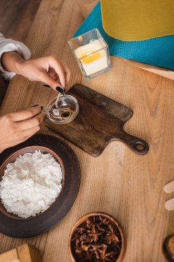 top view of cropped african american woman dipping twine in melted wax near burning candle and wax sheets on wooden table