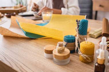 handmade candles near natural ingredients and wax sheets near cropped african american craftswoman on blurred background