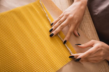top view of cropped african american woman holding candle wick near wax sheet on parchment in craft workshop