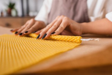 partial view of african american craftswoman making natural candle and rolling wax sheet on blurred parchment in workshop