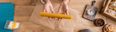 top view of cropped african american woman holding natural handmade candle above craft paper on wooden table, banner