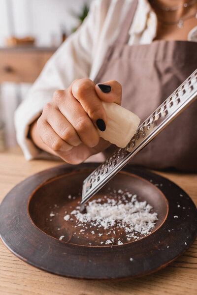 cropped view of african american woman grating soap bar on wooden plate in crafts workshop
