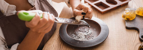 partial view of african american woman grating soap bar on wooden plate in workshop, banner