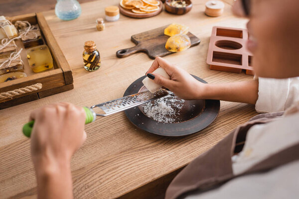 partial view of blurred african american woman with grater near silicone mold and handmade soap on table in workshop