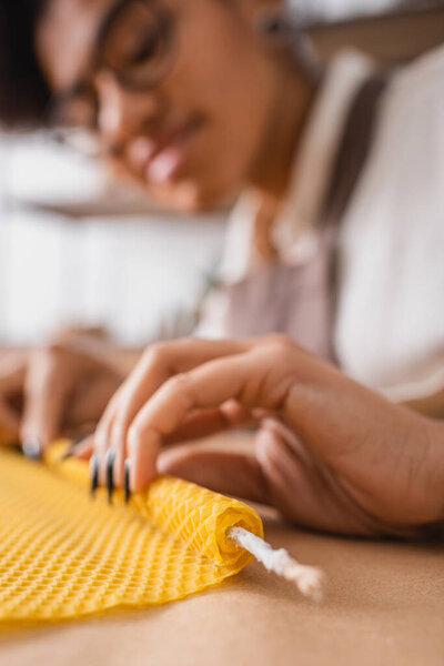 blurred african american woman rolling wax sheet while making candle in craft workshop