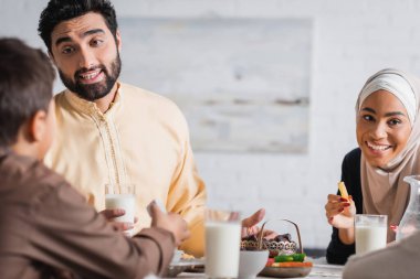 Smiling muslim parents talking to son near suhur food at home 