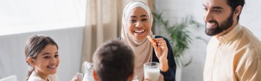 African american woman in hijab holding cevizli sucuk during suhur with family at home, banner 