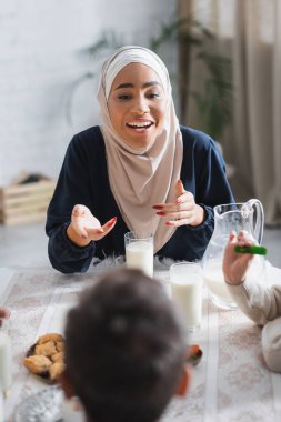 Gülümseyen Afro-Amerikan tesettürlü anne suhur kahvaltısı sırasında çocuklarla konuşuyor. 