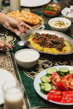Müslüman kadının evdeki iftar yemeğinin yakınındaki masaya pilav koyarkenki görüntüsü. 