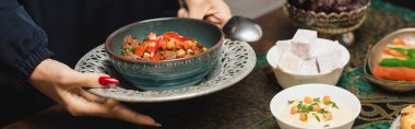 Cropped view of muslim woman holding delicious dish during ramadan dinner, banner 