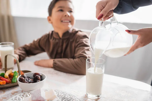 stock image Muslim mother pouring milk during suhur breakfast near blurred son at home 