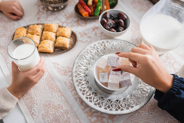 Top view of muslim mother taking turkish delight near son with glass of milk during ramadan 