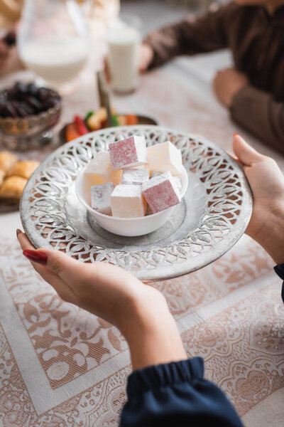 Cropped view of muslim woman holding tasty turkish delight near food during ramadan in morning 