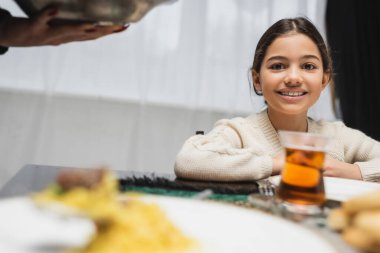 Smiling muslim girl looking at camera near mother and food during ramadan 