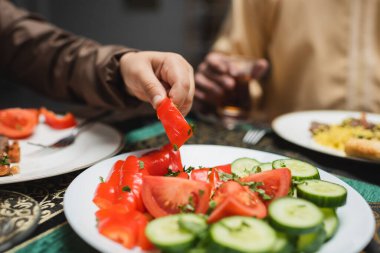 Cropped view of muslim boy taking vegetable during iftar at home  clipart